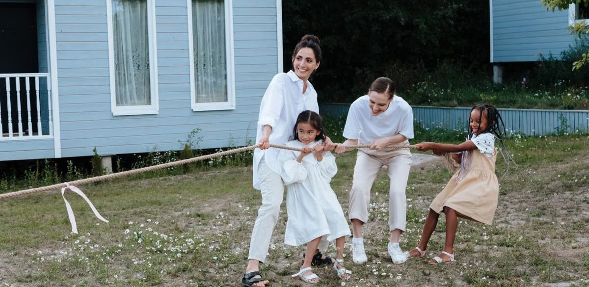A happy family enjoys a game of tug of war in a grassy field by a house.