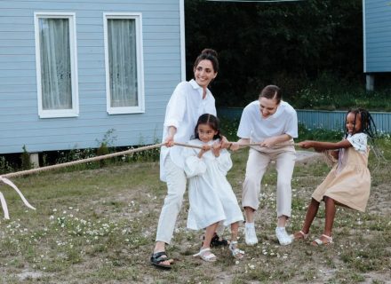 A happy family enjoys a game of tug of war in a grassy field by a house.