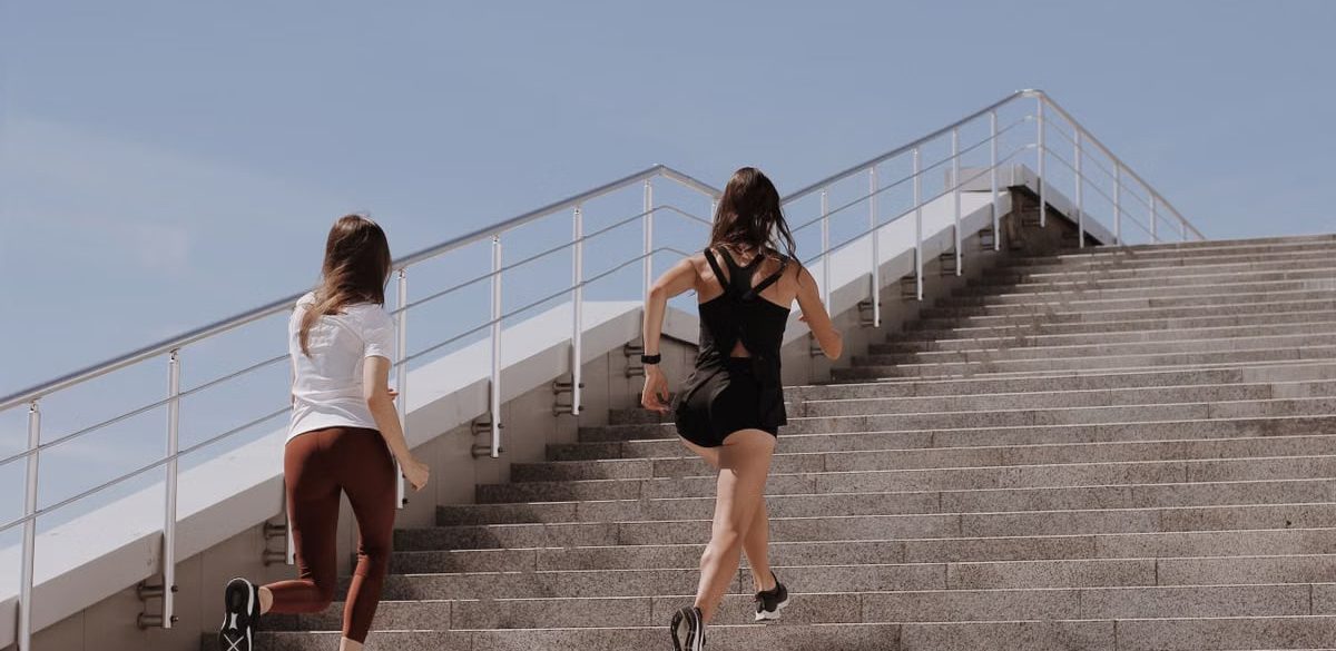 Two women running up stairs outdoors, embodying fitness and wellness.