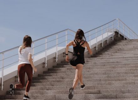 Two women running up stairs outdoors, embodying fitness and wellness.